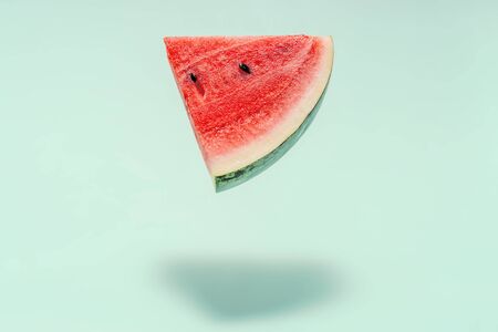 Watermelon slice falling on pastel background. Floating fruits in the air. Flying red fruits. Summer background. Trend colors, copy space.の写真素材