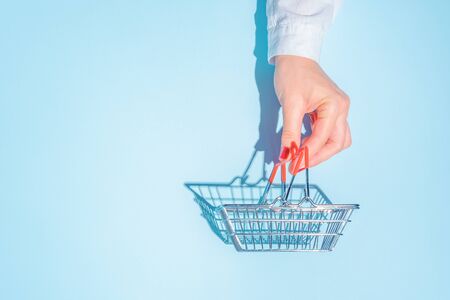 hand holding empty metal shopping basket. Concept of consumerism, shopping symbol. Copy space trend...