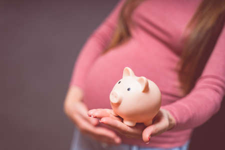 Pregnant woman with piggy bank, saving money to her newborn baby. Money saving, donation, economizing, pregnancy, finance, investment, fund and life insurance concept.の写真素材