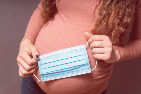 Pregnancy And Infection concept. Pregnant Woman holding Medical Face Mask against flu and viruses. Healthcare conceptの写真素材