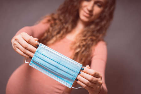 Pregnancy And Infection concept. Pregnant Woman holding Medical Face Mask against flu and viruses....