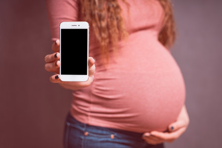 Pregnant woman with smartphone, showing mobile phone with empty blank screen. Smartphone mockup, copy space for mobile applications. Pregnancy, Technology, preparation and expectation concept.の写真素材