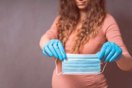 Pregnancy And Infection concept. Pregnant Woman in blue gloves holding Medical Face Mask against flu...