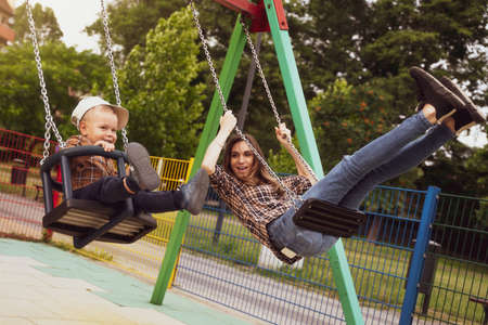 Mother and son on a swing. Happy moment. Mother and son in the park. Active outdoors leisure in city