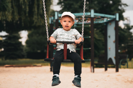Swing children. Little boy having fun on a swing on the playground in public park. Happy child enjoy swinging. Active outdoors leisure for child in city.の写真素材