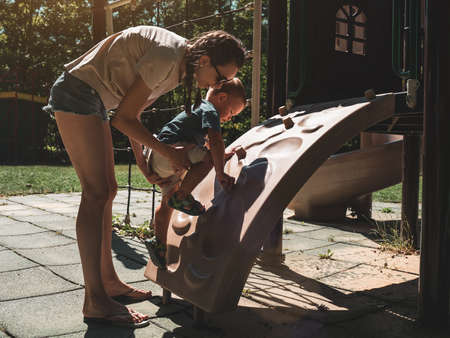 Mother supporting and holding her 2 years old child son on climbing wall at children playground. Mom and son having fun. Support childhood parenthood symbol. Sunny, summer dayの写真素材