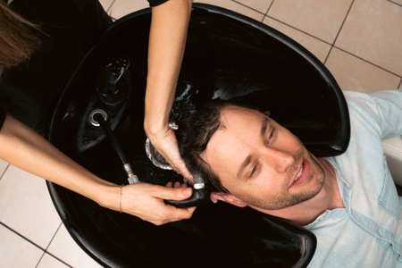 Hair salon master washing client hair at barber shop. Male client getting haircut by hairdresser. Hair care, beauty industry, barber conceptの写真素材