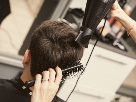 Hair salon master blow dry hair client at barber shop. Mens fashion and style. Hair care, beauty industry, barber concept. Barber shop men hairstyle. Young man getting a modern haircutの写真素材