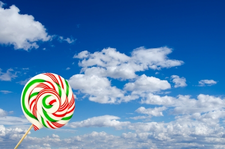 Single sugar lollipop in white green and red on background of sky and cloudsの写真素材