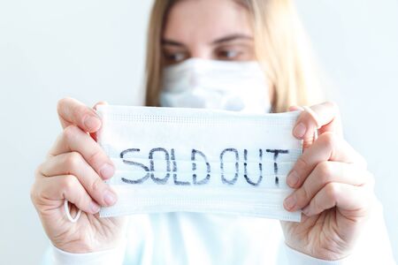Woman in disposable blue medical shirt holds in hands information plate with text: face masks are out of stock, sold out. Epidemic of N-CoV 2019 influenza coronavirus mutated and spreadingの写真素材