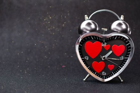 Steel clock alarm in the form of a heart with red hearts inside on a black glitter shiny background. Happy Valentine's Day.の写真素材