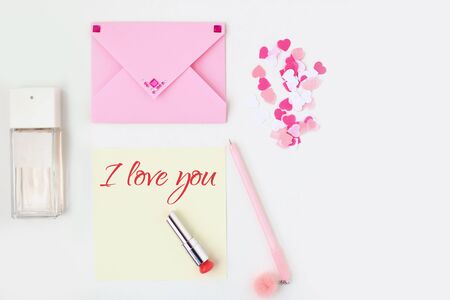 Flat lay: yellow paper, pink envelope, pen, pompom, perfume, lipstick, confetti hearts, lip print, i love you text. Making postcard in envelope for Valentine's Day.Do it yourself.Photo from the seriesの写真素材