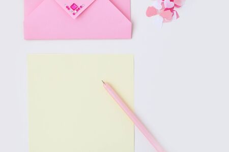 Flat lay: yellow paper, pink envelope with rhinestones, pen, pompom, confetti hearts. Making...