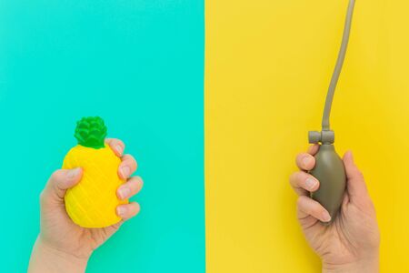 Flat lay stress, antistress: toy squish yellow pineapple in hand, blood pressure monitor.Bright blue background.Compressing, soft,squeezable items to relieve,problems,anxieties,worries.Summer concept.の写真素材