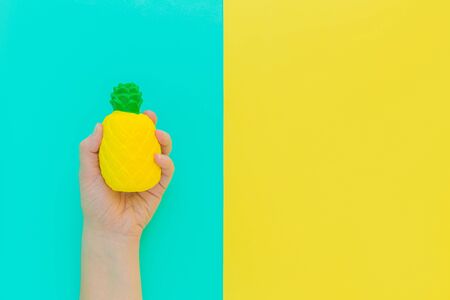 Flat lay antistress toy squish yellow pineapple with green leaves in hand.Bright blue background.Compressing, soft, squeezable items to relieve stress, problems, anxieties, worries. Summer concept.の写真素材