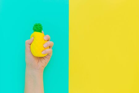 Flat lay antistress toy squish yellow pineapple with green leaves in hand.Bright blue background.Compressing, soft, squeezable items to relieve stress, problems, anxieties, worries. Summer concept.の写真素材
