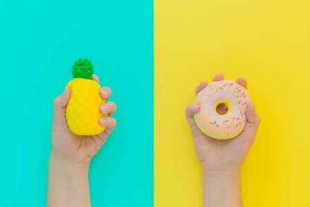 Flat lay antistress squish toys yellow pineapple,pink donut with sprinkles in hands.Bright blue background.Compressing,soft,squeezable items to relieve stress,problem,anxieties,worries.Summer concept.の写真素材