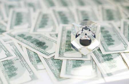 Drop of black oil of Brent brand in crystal cube laying on the background of hundred dollars bills....