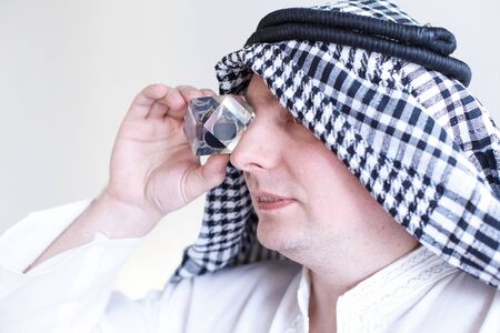 Arab sheikh from Arabia saudi,Emirates holds in hands and looks to drop of black oil of Brent brand in crystal cube.Crisis in financial market, falling,rising prices, quotes, changes in exchange rate.の写真素材