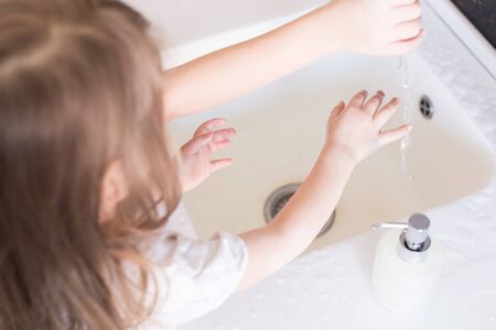 Little girls wash their hands in the sink with soap in the foam. Protection against coronovirus...