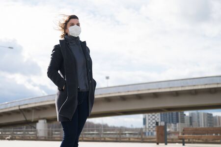 Fashionable stylish scared woman in protective blue face mask, gray wool coat on the street near...