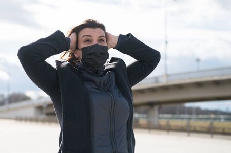Fashionable stylish scared woman in protective black face mask, gray wool coat on street near metro...