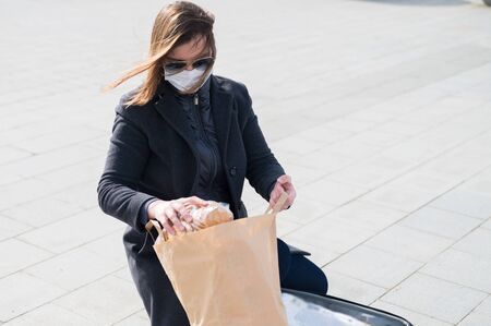 Scared woman in protective face mask,gray coat.Making store of food in suitcase before isolation:toilet paper,paste,cookies.Lack of products.Leaving city during quarantine from coronavirus covid-2019.の写真素材