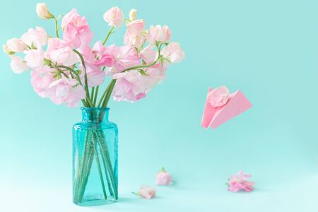 Bouquet of pink sweet peas Lathyrus in beautiful transparent vase on blue background.Paper airplane with message. Spring concept. International Women's Day, March 8 and Valentine's Day,14 of February.の写真素材