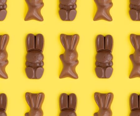 Easter bunny shaped sweets of milk chocolate laying in rows on yellow background.Religious holiday composition,rabbit pattern for congratulations, greeting card.Symbol of celebration Sunday of Christ.の写真素材
