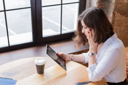 Business woman in white shirt working at tablet at home office,drinking coffee.Distance...