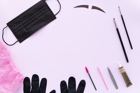 Flat lay. Accessories for shaping and dyeing eyebrows. Black mask, brushes, black gloves, pink hat, henna, paint on a pink backgroundの写真素材