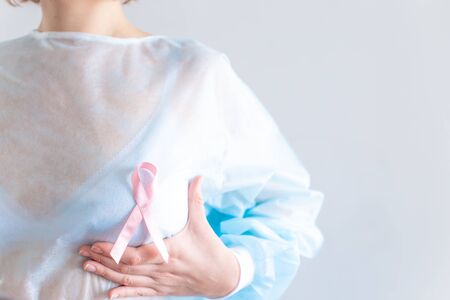 International cancer day. A woman with short blond hair, in a disposable medical blue shirt, in a white bra holds her hand over her breast. Pink ribbon.の写真素材