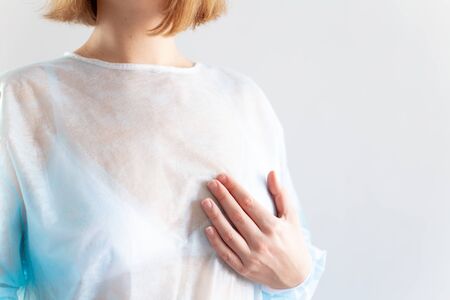 International cancer Day. A woman with short blond hair, in a disposable medical blue shirt, in a white bra holds her hand over her breast.の写真素材