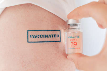 Vial with vaccine for covid-19 coronavirus, flu, infectious diseases. Patient hand with blue stamp...