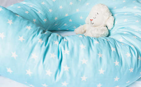 Light blue supporting pillow with stars on white sheet in bed for comfortable sleep of pregnant woman. Funny sleeping toy sheep, lamb. Goods, accessories for expectant mothers, kids, baby.の写真素材