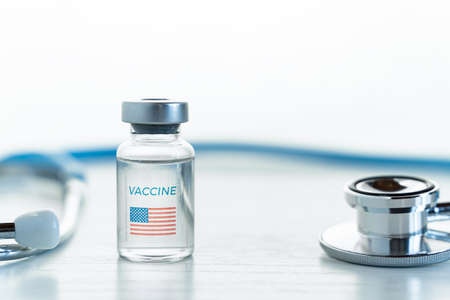 Transparent vial with USA, american flag. Vaccine for covid-19 coronavirus, flu, infectious diseases. Phonendoscope. Injection after clinical trials for vaccination of human, people. Medicine, drug concept.の写真素材