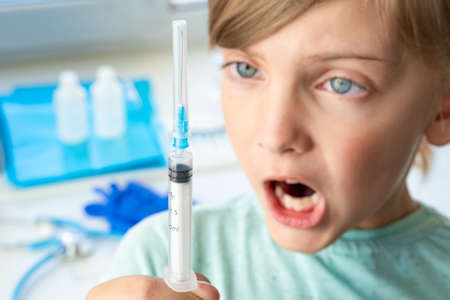 Little girl in doctor's office is afraid of syringe with vaccine. Vaccination for covid-19 coronavirus, flu, dangerous infectious diseases. Injection, clinical trials for human, child. Medicine concept.の写真素材