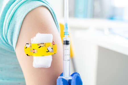 Vaccination of little girl in doctor's office. Kids funny adhesive plaster, gauze napkin Syringe with vaccine for covid-19 coronavirus, flu, infectious diseases. njection.Clinical trials for human, child.の写真素材