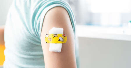 Vaccination of little girl in doctor's office.Kids funny adhesive plaster, gauze napkin.Sits on chair.Vaccine for covid-19 coronavirus, flu, infectious diseases.Injection.Clinical trials for human, child.の写真素材