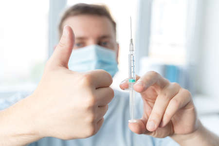 Man, adult in face mask in doctor's office is vaccinated. Syringe with vaccine for covid-19 coronavirus, flu, dangerous infectious diseases. Injection after clinical trials for human, child. Medicine.の写真素材