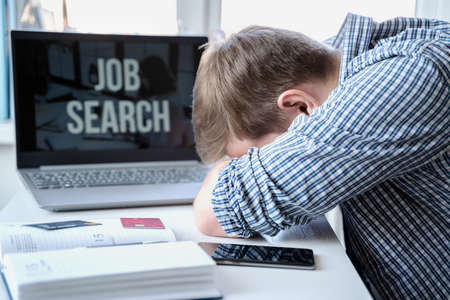 Man lies face down on table next to laptop. Unemployment, crisis, stress, job loss. Looking for remote work at home.Mobile phone, organizer, empty credit cards.Hiring employees, freelancers for telework.の写真素材