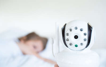 Camera near a little sleeping girl, daughter. Radio, video baby monitor. Protection, care for the safety of the child. Remote control of the soap. Modern technologies.の写真素材