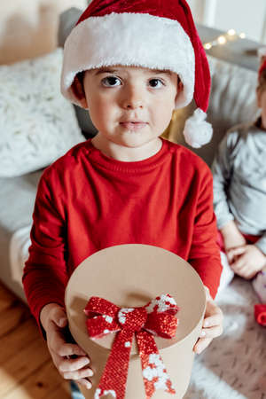 Little cute happy boy, kid in red Christmas santa claus hat with gift in hands from family, parents....