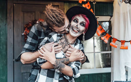 Scary love couple. Terrifying black skull face makeup. Witch costumes, stylish images.Horror, fun at children's party in barn on street.Hats, jackets.の写真素材