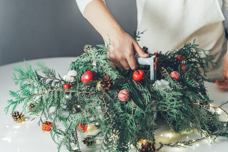 Florist woman makes Christmas composition for table decoration from thuja, spruce branches in wooden box.の写真素材