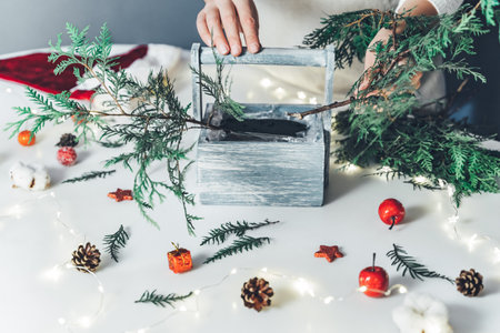 Florist woman makes Christmas composition for table decoration from thuja, spruce branches in wooden box.の写真素材