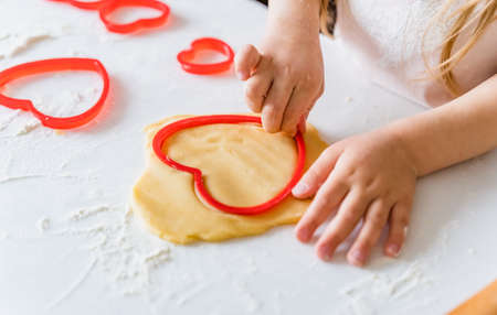 Little girls, sisters cooking homemade heart shaped cookies for valentine's day. Holiday for all lovers. Gift, surprize for mom. Red molds, rolling pin, flour, dough.Handmade family, bakery with kids.の写真素材