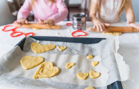 Little girls, sisters cooking homemade heart shaped cookies for valentine's day. Holiday for all lovers. Gift, surprize for mom. Red molds, rolling pin, flour, dough.Handmade family, bakery with kids.の写真素材