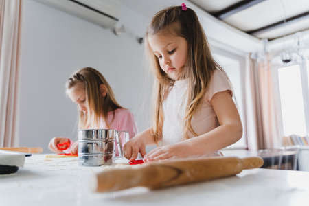 Little girls, sisters cooking homemade heart shaped cookies for valentine's day. Holiday for all...