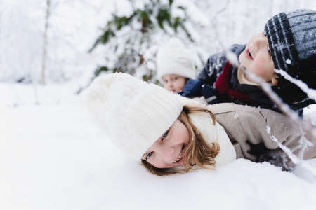 Family fun,winter kids activity in snowy clothes with mom.Children lay in heap on top of each other.Happy cute boys,girls.Walking in beautiful forest,park.Snowy trees.Hat,coat,scarf.Fashionable image.の写真素材